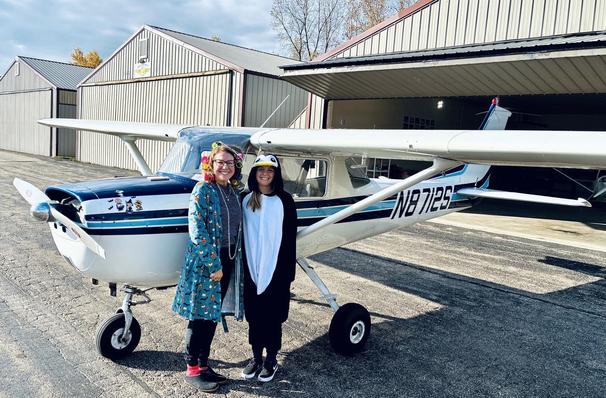 Mary Shandonay standing by her airplane with her flight instructor, Kylee, both dressed in Halloween costumes.